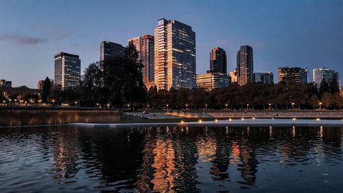 Illuminated city by lake against sky