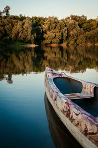 Boat moored on lake by trees against sky