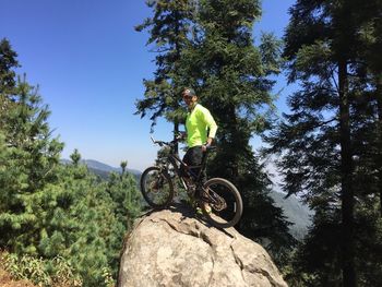 Male hiker standing with bicycle on rock at forest