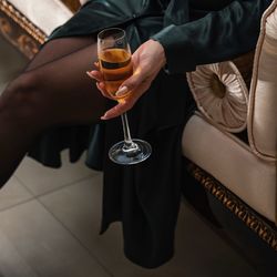 Midsection of woman holding champagne flute while sitting on sofa