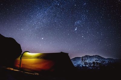 Illuminated tent on field against sky with star field