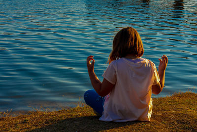 Rear view of girl meditating while sitting by lake