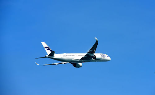 Low angle view of airplane flying against clear blue sky