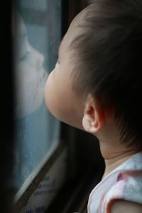 Close-up of boy looking at his reflection in window