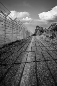 Shadow of fence on bridge against sky
