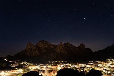 Illuminated town by mountains against sky at night