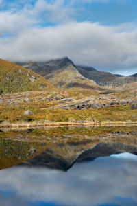 Mountain and autumnal forest under the sky reflecting in surface of water in norway.