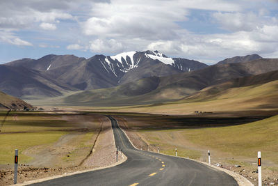 A flat,wide asphalt road leads to the beautiful and spectacular snow mountains in the distance