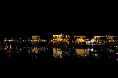 Illuminated buildings by river against sky at night