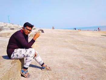 Full length of man sitting on rock against sky