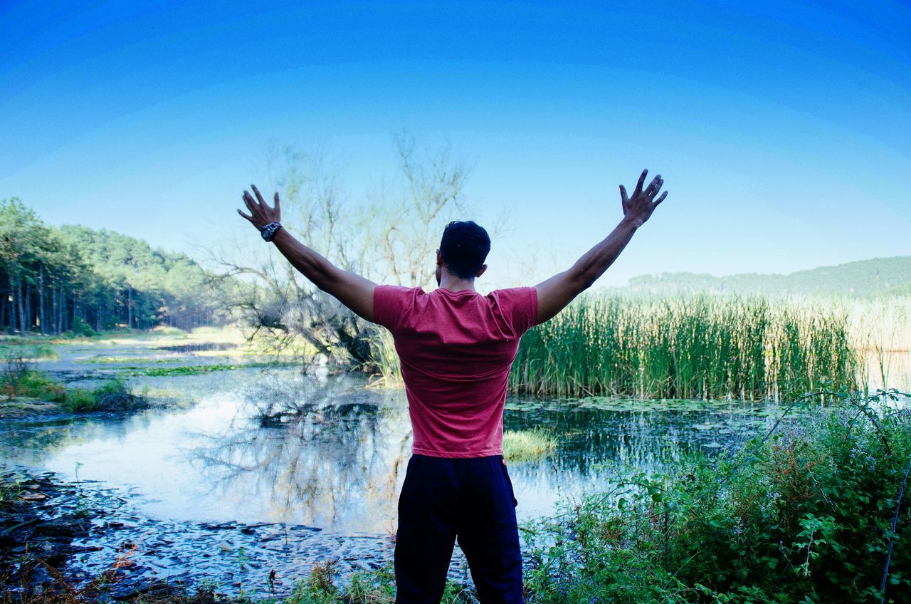 water, leisure activity, lifestyles, standing, blue, clear sky, tranquil scene, tranquility, rear view, full length, casual clothing, beauty in nature, scenics, nature, three quarter length, sky, tree, vacations