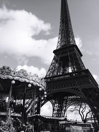 Low angle view of eiffel tower and carousel against cloudy sky in city