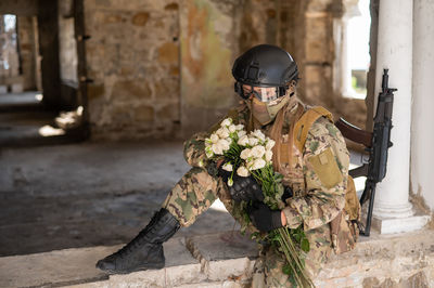 Soldier holding flower while sitting on wall