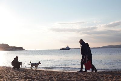 People with dog on beach against sky