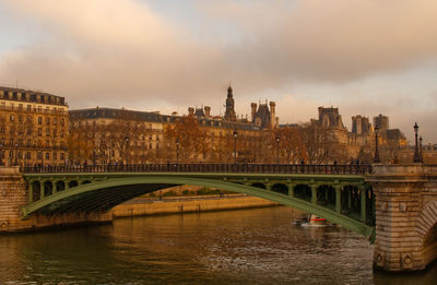 Bridge over river in city against cloudy sky