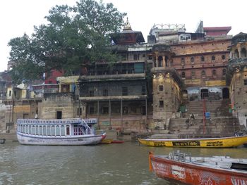 Boats in river by buildings against sky