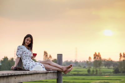 Portrait of smiling young woman sitting against sky during sunset