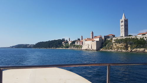 Scenic view of sea by buildings against clear blue sky