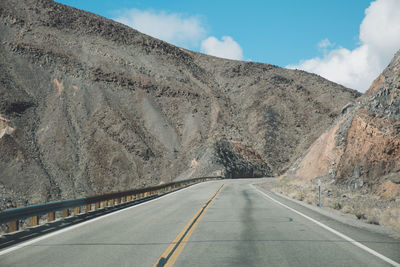 Empty road by mountains against sky