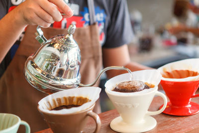 Close-up of hand holding pouring coffee in cups on table