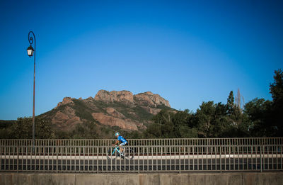 Man riding bicycle on road against clear blue sky