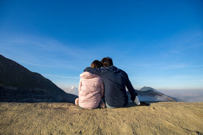 Rear view of couple sitting on land against sky