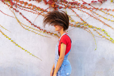 Side view of young cheerful female with flying hair standing near stone wall