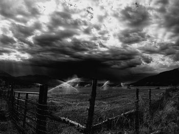 Fence on field against storm clouds