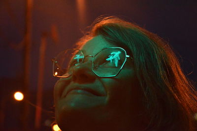 Close-up of smiling woman wearing eyeglasses looking up at night