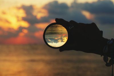 Cropped hand holding crystal ball against sky during sunset