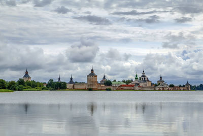 View of buildings by lake against cloudy sky