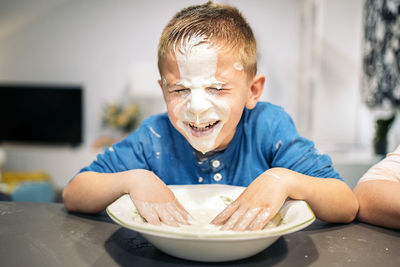 Smiling boy smearing face in flour and water at home