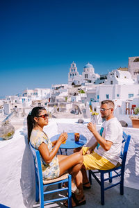 People sitting on seat against cityscape and blue sky