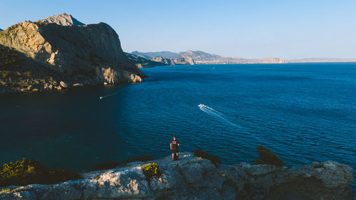 Rear view of man standing on rock against sea and sky