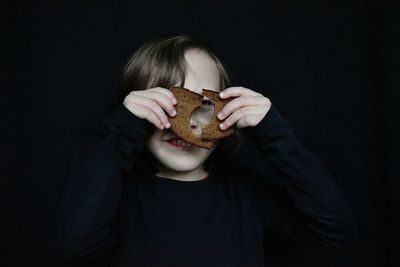 Close-up of girl holding bread against black background