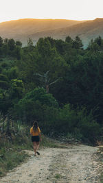 Rear view of woman walking on dirt road against trees