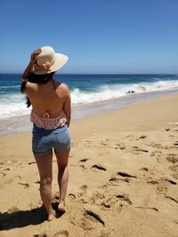 Rear view full length of young woman standing on shore at beach during sunny day