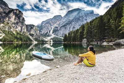 Woman sitting on lakeshore against mountains