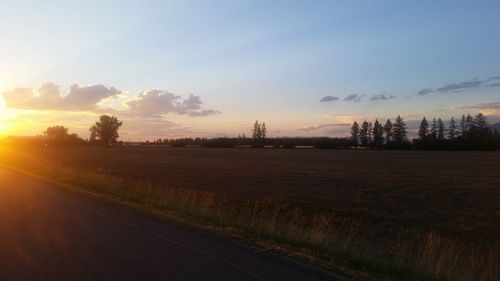 Road by agricultural field against sky during sunset