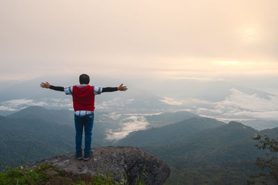 Asian man with freedom arms open standing on rock ledge of mountain peak at pha tang view point 104 