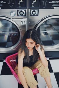 High angle view of woman sitting in basket by washing machine