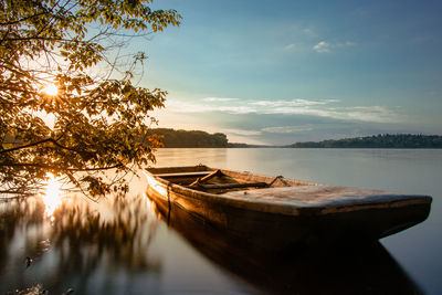 Fairy-tale boat moored on shore of dam with the setting sun coming through tree illuminates scenery