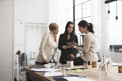 Happy businesswomen looking at digital tablet while standing in office