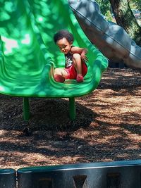 Full length of boy sitting on slide at playground