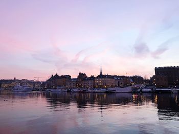 Buildings by river against sky at sunset