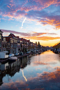 Boats moored in canal by buildings against sky during sunset