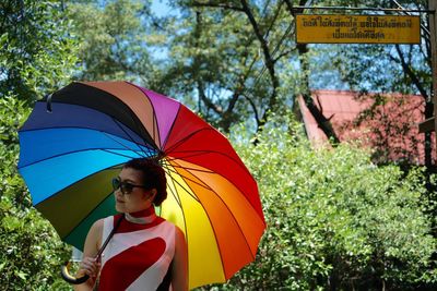 Woman holding colorful umbrella while standing against plants