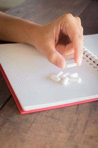 Cropped hand of person holding medicine on spiral notebook