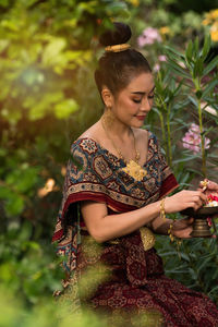 Beautiful woman holding flowers in hand against plants