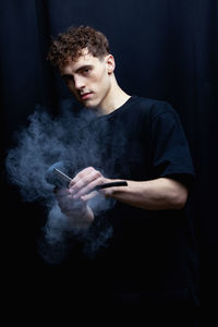 Portrait of young man with arms crossed against black background